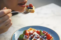 Vrouw eet versgebakken wafel met fruit en poedersuiker op een blauw bord