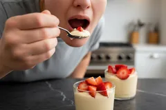 Persoon eet yoghurt met aardbeien uit een glas in de keuken. Gezond dessert moment.