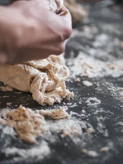 Persoon houdt wit pizzadeeg vast op zwarte tafel