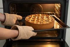 Verse appeltaart wordt uit de oven gehaald met ovenwanten, heerlijke zelfgebakken taart.