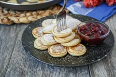 Poffertjes op een bord met poedersuiker en kersencompote, Nederlandse lekkernij ontbijt.