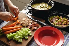 Ingrediënten snijden voor Hollandse erwtensoep met groenten en worst op houten plank.