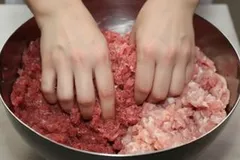 Twee handen mengen gehakt in een kom, rood en licht gemengd vlees, keukenvoorbereiding