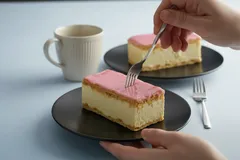 Twee tompoucen op zwarte borden met een kop koffie, hand prikt met vork in gebak.