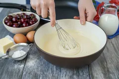 Ingrediënten voor het bakken: beslag mixen, kersen, eieren, melk, boter en suiker op tafel.