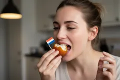 Vrouw eet Nederlandse oliebol met vlaggetje, typisch Hollands gebak, binnen in huis.